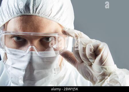 Foto ritratto di medic in guanti. costume e maschera che regge occhiali protettivi. Foto Stock