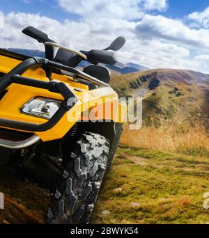 Foto di un veicolo atv giallo fuoristrada in piedi su un sentiero in montagna in primo piano con protezione della ruota anteriore. Foto Stock