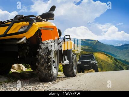 Foto di un atv giallo fuoristrada e di veicoli trick in piedi su una vista frontale della strada di montagna. Foto Stock