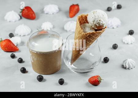 gelato in un cono di waffle su uno sfondo chiaro. Il gelato si sta sciogliendo. Cialde e fragole sullo sfondo Foto Stock