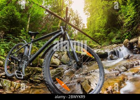 Foto di una mountain bike che si erge su un paesaggio di un torrente di foresta, vista ravvicinata delle ruote. Foto Stock