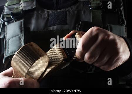 Foto di un soldato completamente attrezzato in gilet tattico con armatura nera in piedi con cintura su sfondo nero vista frontale closeup. Foto Stock