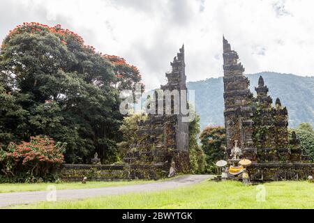 Tradizionale balinese a porte divise candi bentar. Bedugul, Gianyar, Bali, Indonesia. Spathodea Campanulata, o tulipani africani intorno. Foto Stock