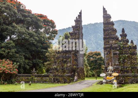 Tradizionale balinese a porte divise candi bentar. Bedugul, Gianyar, Bali, Indonesia. Spathodea Campanulata, o tulipani africani intorno. Foto Stock