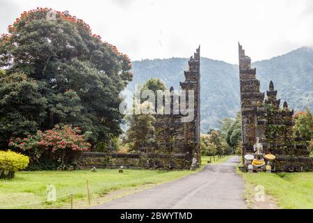 Tradizionale balinese a porte divise candi bentar. Bedugul, Gianyar, Bali, Indonesia. Spathodea Campanulata, o tulipani africani intorno. Foto Stock