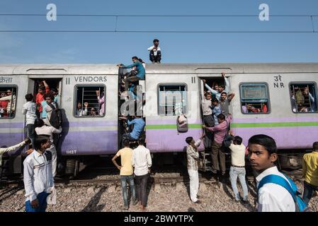 I pendolari si aggirano tra le ferrovie e si siedono sul tetto di un treno sovraffollato delle ferrovie indiane, alla stazione ferroviaria di Noli vicino a Ghaziabad, Nuova Delhi, in Foto Stock