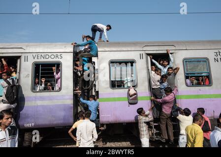 I pendolari si aggirano tra le ferrovie e si siedono sul tetto di un treno sovraffollato delle ferrovie indiane, alla stazione ferroviaria di Noli vicino a Ghaziabad, Nuova Delhi, in Foto Stock