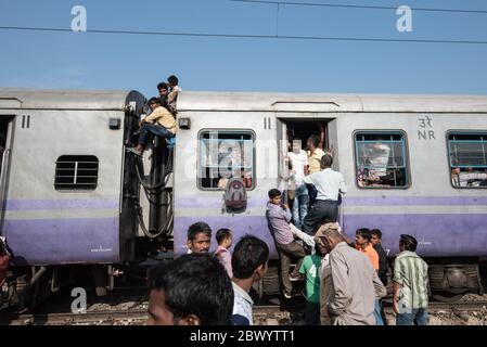 I pendolari si aggirano tra le ferrovie e si siedono sul tetto di un treno sovraffollato delle ferrovie indiane, alla stazione ferroviaria di Noli vicino a Ghaziabad, Nuova Delhi, in Foto Stock