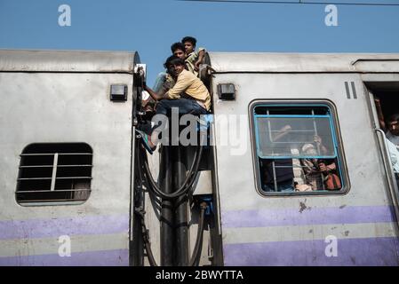 I pendolari si aggirano tra le ferrovie e si siedono sul tetto di un treno sovraffollato delle ferrovie indiane, alla stazione ferroviaria di Noli vicino a Ghaziabad, Nuova Delhi, in Foto Stock