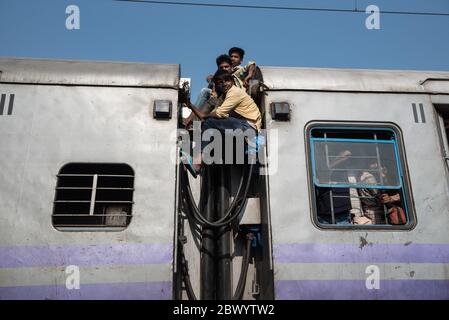 I pendolari si aggirano tra le ferrovie e si siedono sul tetto di un treno sovraffollato delle ferrovie indiane, alla stazione ferroviaria di Noli vicino a Ghaziabad, Nuova Delhi, in Foto Stock