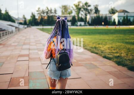 Giovane bella ragazza in una T-shirt gialla sta camminando all'aperto nello stadio sportivo studentessa torna a scuola Foto Stock