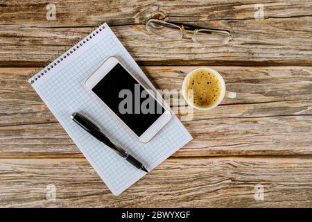 Libro di note vuoto con notebook a spirale e tazza di caffè a matita per smartphone su sfondo di legno Foto Stock