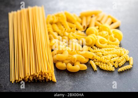 Vari tipi di pasta italiana cruda su tavola nera. Foto Stock