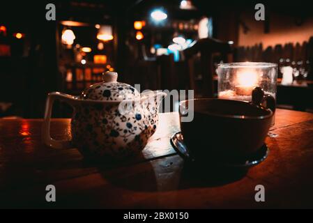 Una teiera, una tazza e una tealight all'interno di un bicchiere sopra un tavolo di legno di un accogliente pub irlandese Foto Stock