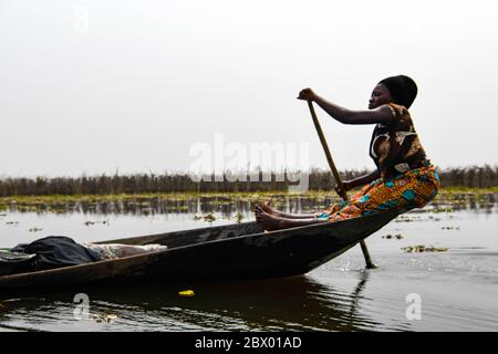 Africa, Africa occidentale, Benin, Lago Nokoue, Ganvié. Donna che canottava sul retro di una piroga fuori dalla città sul lago di Ganvié sul lago Nokoue. Foto Stock