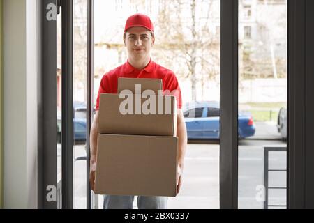 Ordini online e moderno servizio postale. Il corriere in uniforme rossa contiene molte scatole Foto Stock