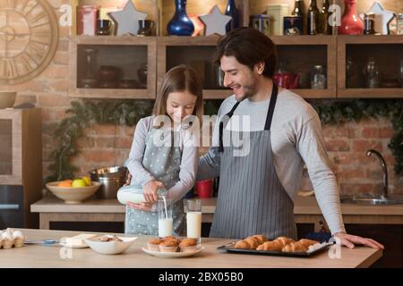 Papà e bambina gustano muffin fatti in casa e latte in cucina Foto Stock