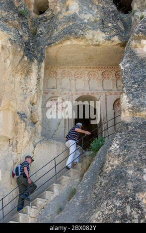 I visitatori del Museo all'aperto di Goreme nella regione della Cappadocia in Turchia salgono le scale per entrare nell'antica chiesa di Santa Barbara. Foto Stock