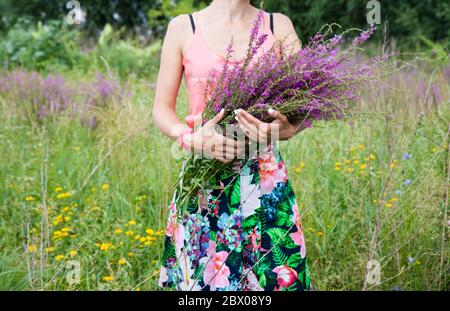 Una giovane ragazza che tiene in mano un bouquet di fiori selvatici. Foto Stock