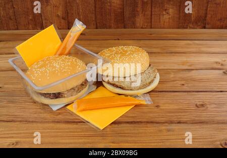 Due hamburger di manzo al forno a microonde con formaggio e salsa su sfondo di legno Foto Stock