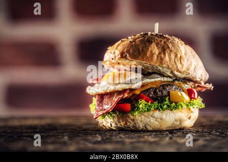 Hamburger con manzo, uova, pancetta, insalata, peperoni in un ambiente rustico Foto Stock