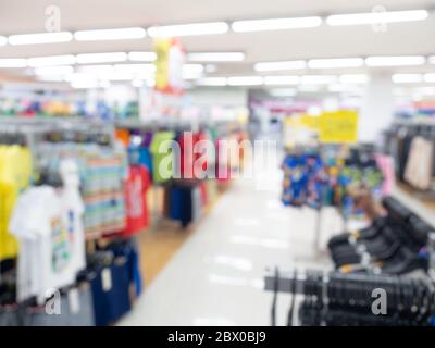Sfondo sfocato supermercato. Vista interna offuscata con passaggio pedonale intorno con abiti appesi nel centro commerciale. Foto Stock