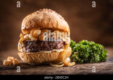 Hamburger di manzo con formaggio fuso, cipolle caramellate in un panino di sesamo con insalata sul lato Foto Stock