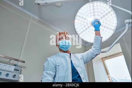 un chirurgo mascherato contro una lampada nella sala operatoria Foto Stock