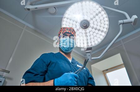 un chirurgo mascherato contro una lampada nella sala operatoria Foto Stock