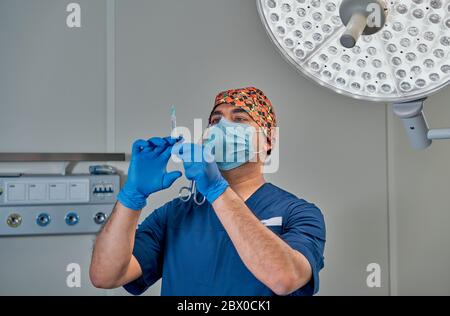 un chirurgo mascherato contro una lampada nella sala operatoria Foto Stock