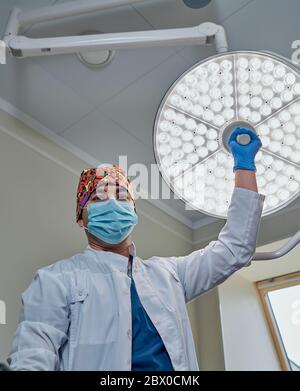 un chirurgo mascherato contro una lampada nella sala operatoria Foto Stock