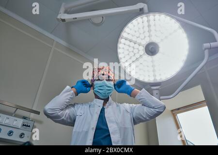 un chirurgo mascherato contro una lampada nella sala operatoria Foto Stock