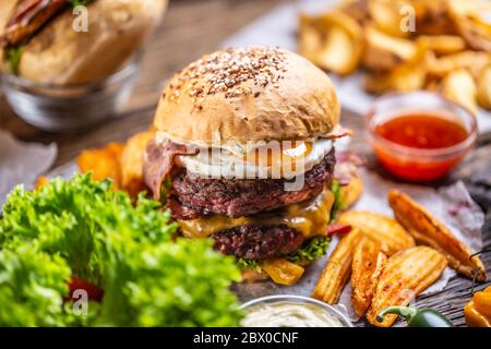 Hamburger doppio di manzo con pancetta e formaggio e lattuga, patatine e salsa su un lato Foto Stock