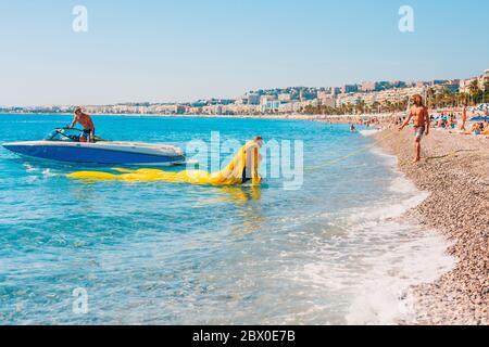 Nizza, PROVENZA / Francia - 29 Settembre 2018: due forti conciate uomini tirare un grande giallo per paracadute parasailing dall'acqua a terra Foto Stock