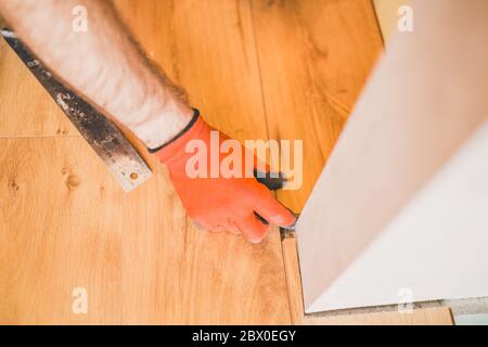 Un lavoratore installa un pavimento laminato durante il lavoro di finitura Foto Stock