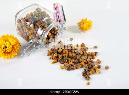 Medicina alternativa, pane di api fatto di miele domestico (fiore fermentato e polline di pianta) all'interno di un piccolo vaso di vetro e sparso su tavola bianca. Foto Stock