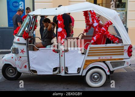 Gallipoli, Italia - 28 giugno 2019: Turisti nelle caratteristiche vie del centro storico di Gallipoli. Alcuni utilizzano una moto speciale a tre ruote Foto Stock