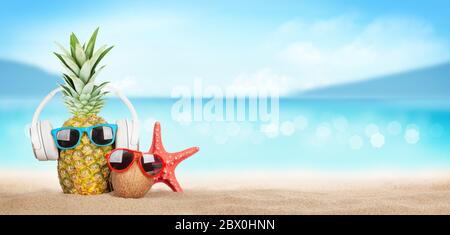 Estate mare tropicale con onde scintillanti, ananas e cocco con occhiali da sole e cuffie sulla spiaggia di sabbia calda. Concetto di viaggio e vacanza con poliziotto Foto Stock