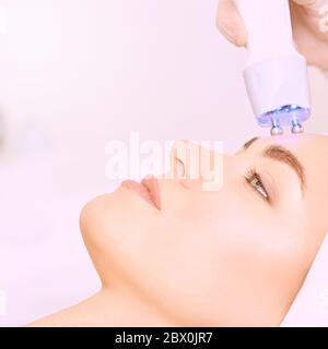 Procedura di estetica della luce microcorrente. Bellezza faccia ragazza. Macchina cosmetologica. Mani del medico. Due micro sfere. Riduzione delle rughe Foto Stock