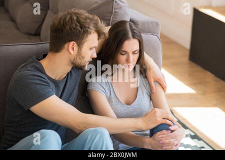 Giovane bella donna che guarda turbato mentre suo marito la abbracciava e parla Foto Stock