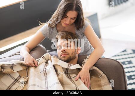 Giovane donna dai capelli scuri che ricopre il marito con una plaid Foto Stock