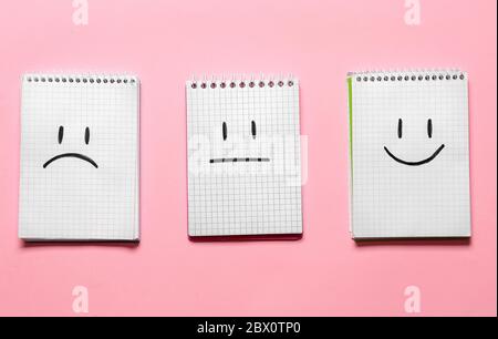 Notebook con volti tristi, felici e neutri disegnati su sfondo a colori Foto Stock