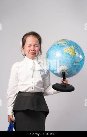 la ragazza di scuola di primo grado in una camicia bianca tiene a. globo nelle sue mani e piange Foto Stock