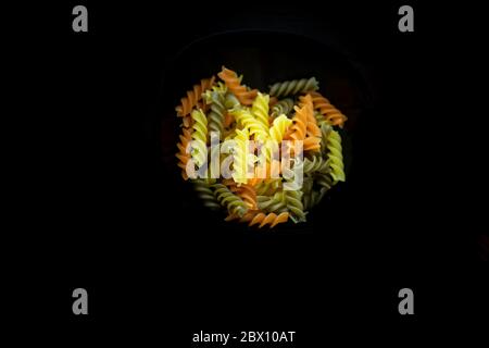 Composizione di fusilli tricolori crudi, a forma di torcente. Primo piano e fuoco selettivo sulla pasta colorata di fusilli, isolata su nero Foto Stock