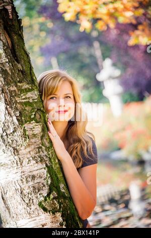 Giovane donna che si nasconde dietro l'albero nel parco autunnale. Giardino giapponese della città Foto Stock