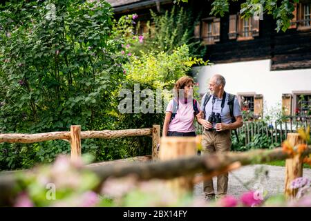 Una coppia di pensionati con binocoli che camminano, parlando. Foto Stock