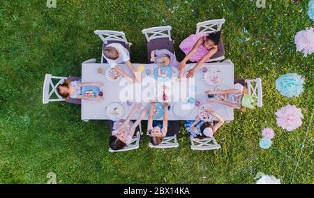 Vista dall'alto dei bambini piccoli seduti al tavolo all'aperto durante la festa in giardino. Foto Stock