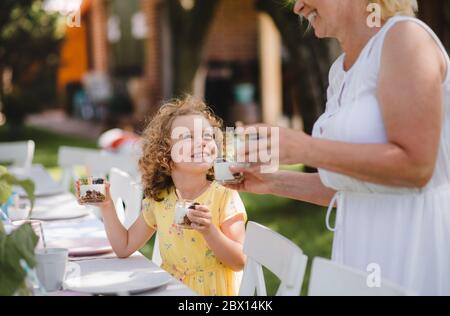 Piccola ragazza con nonna all'aperto in giardino festa in estate, mangiare. Foto Stock