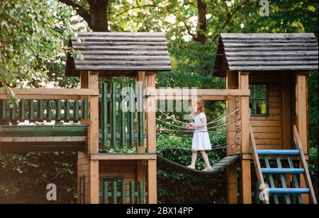 Piccola ragazza all'aperto su parco giochi in legno in giardino in estate, giocando. Foto Stock