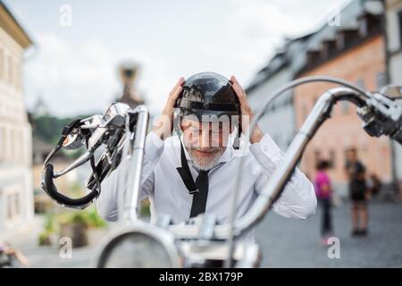 Un uomo d'affari anziano con moto in città, mettendo sul casco. Foto Stock